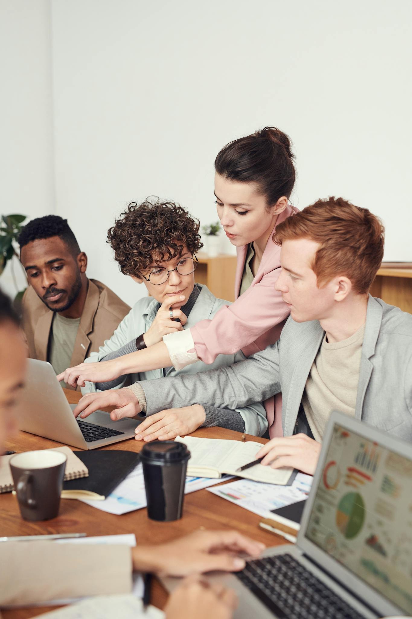 A group of digital professionals engaged in a collaborative office meeting, discussing digital project ideas with laptops.